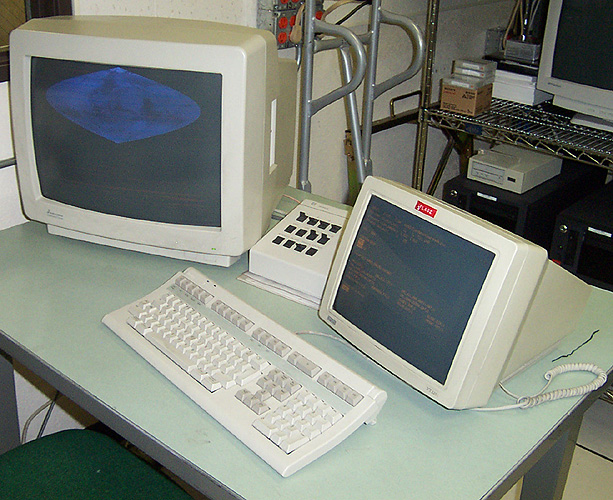 A graphics display screen, a box with twelve switches, and a text-terminal screen sitting behind a keyboard.